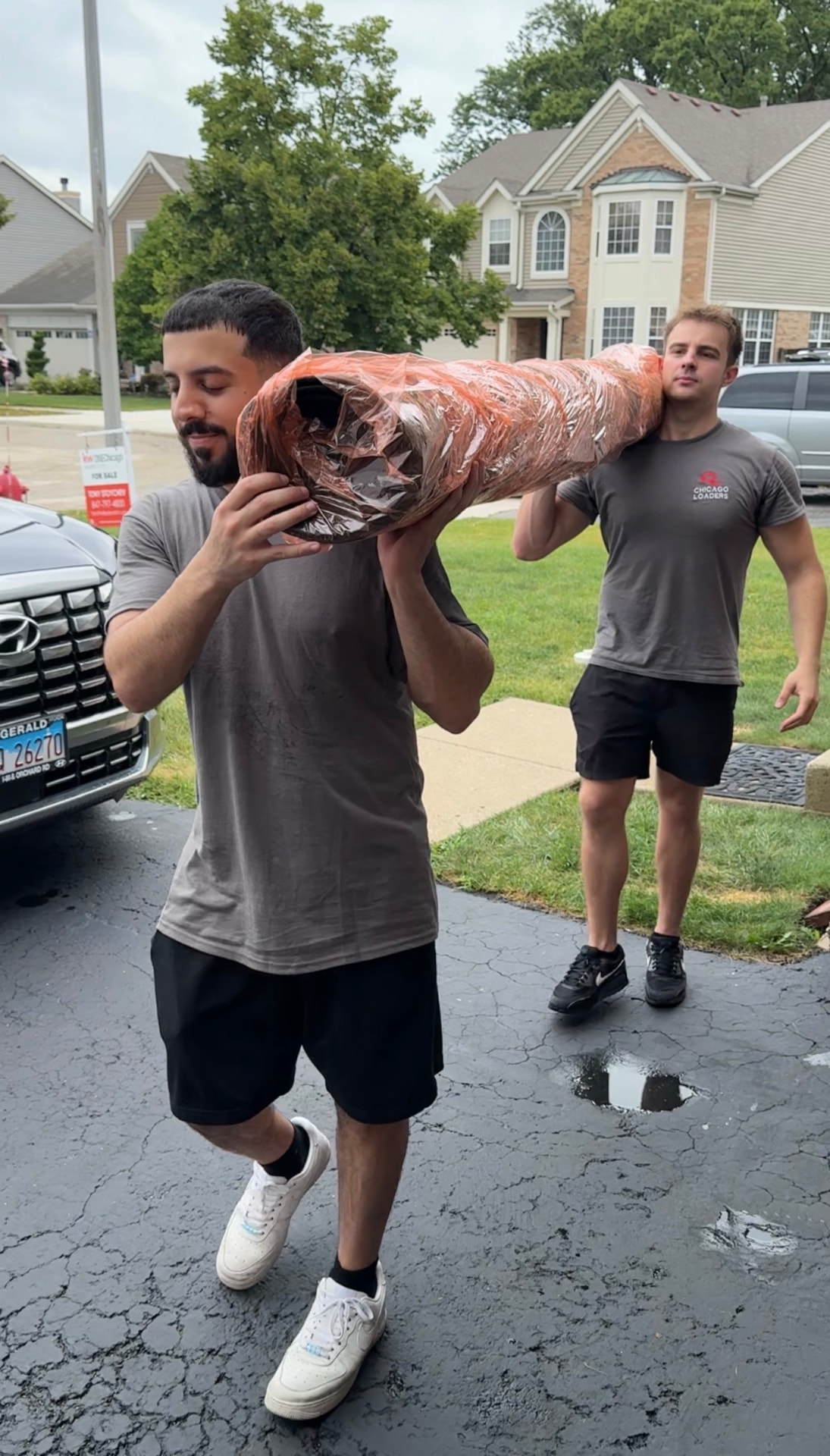 Two movers carrying a shrink-wrapped couch cushion out of a home