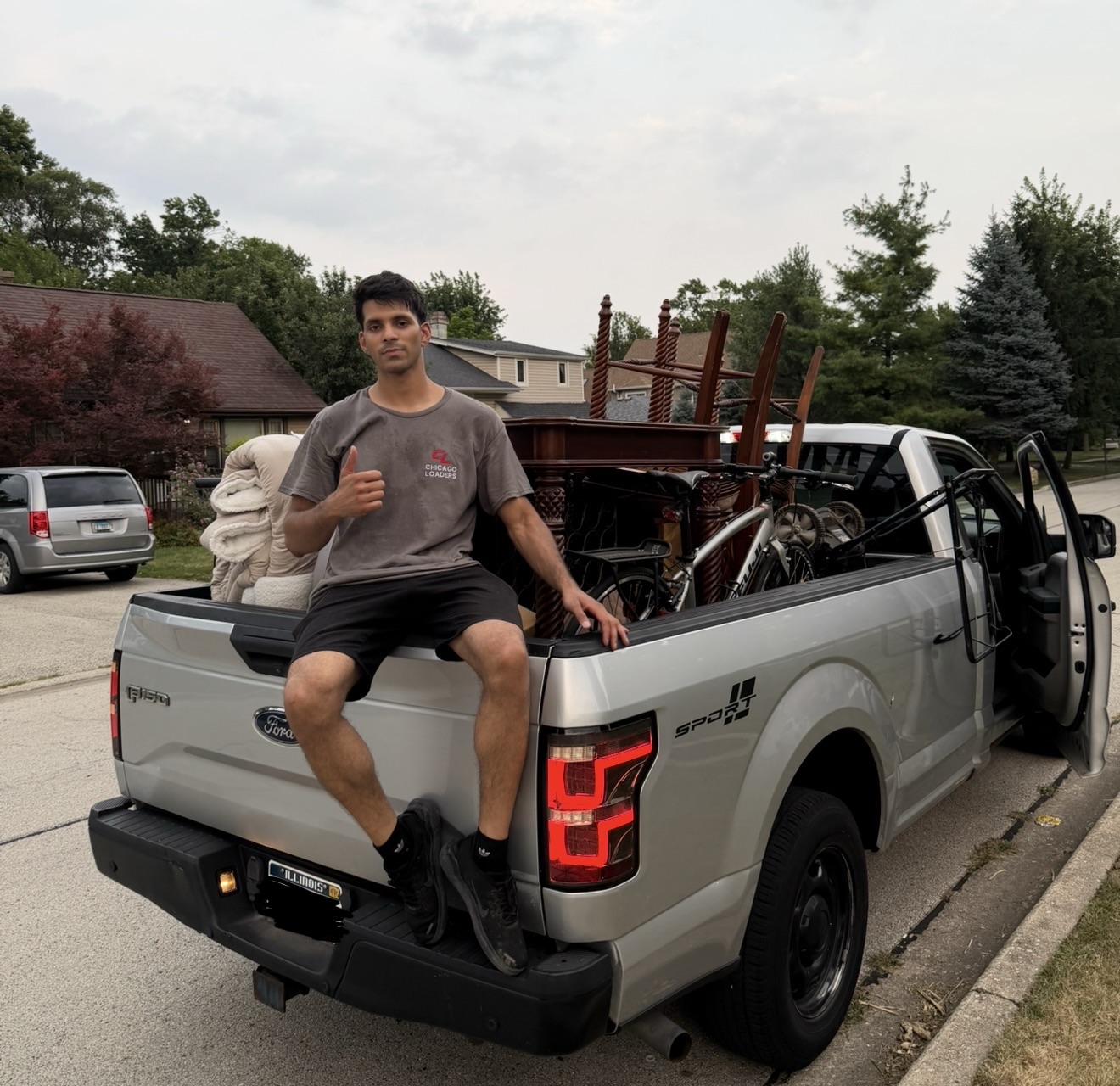 Mover sitting on the tailgate of a pickup truck loaded with furniture and giving a thumbs up