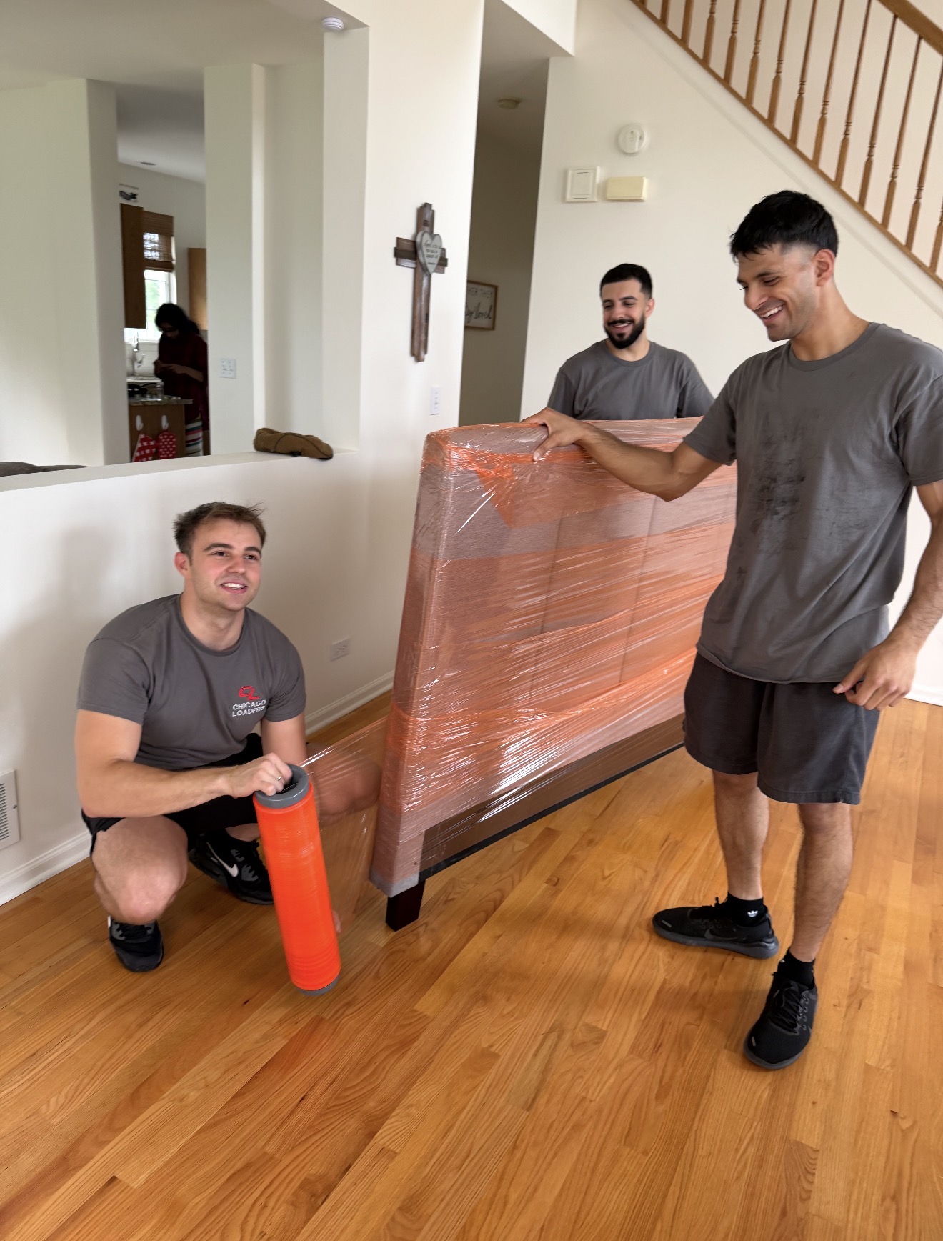 Three Chicago Loaders team members wrapping a mattress in protective plastic inside a home