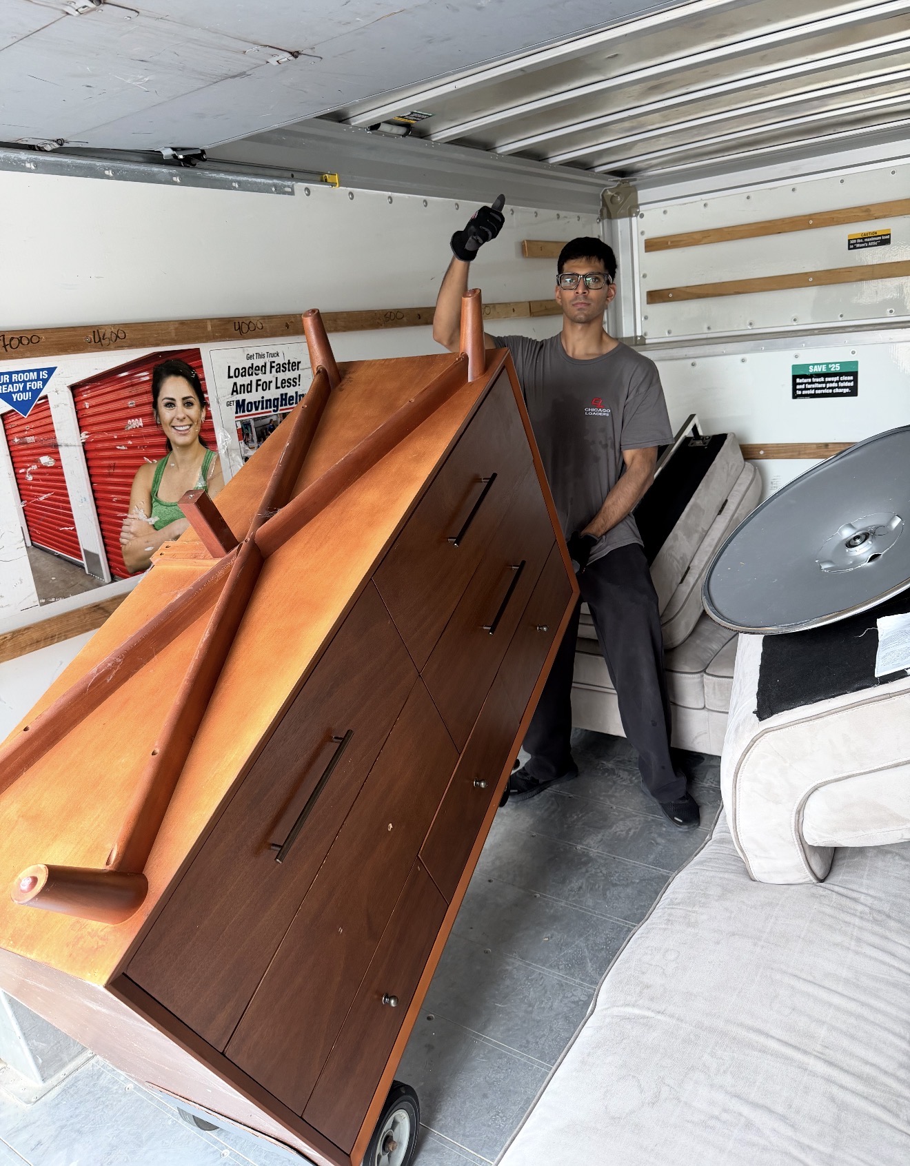 Mover giving a thumbs up while securing a large wooden dresser in a truck